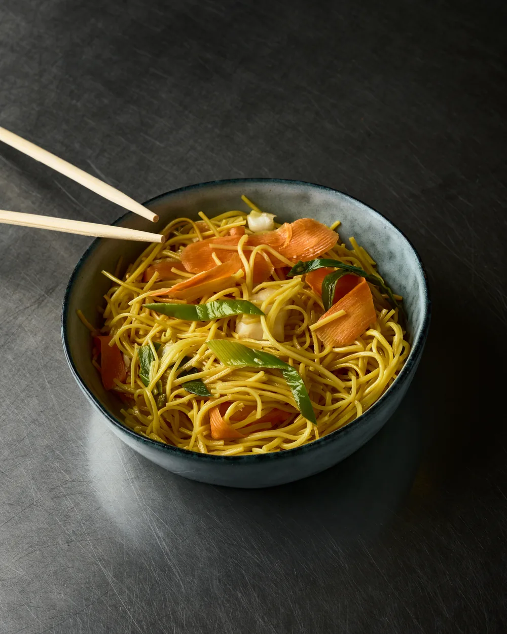 Nouilles sautées aux légumes et aux crevettes, baguettes posées sur le bol
