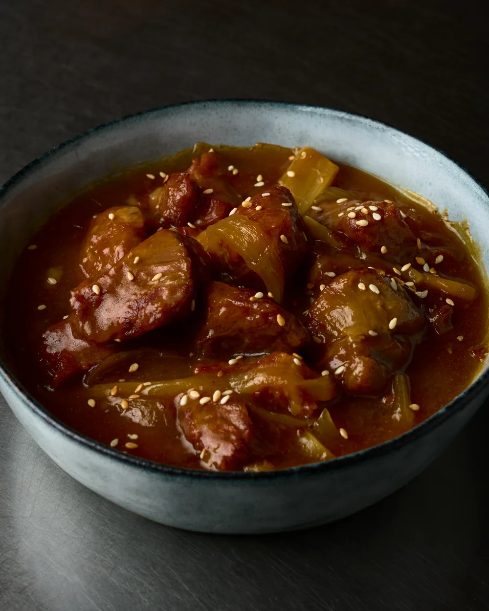 Gros plan sur un plat mijoté en sauce, parsemé de graines de sésame
