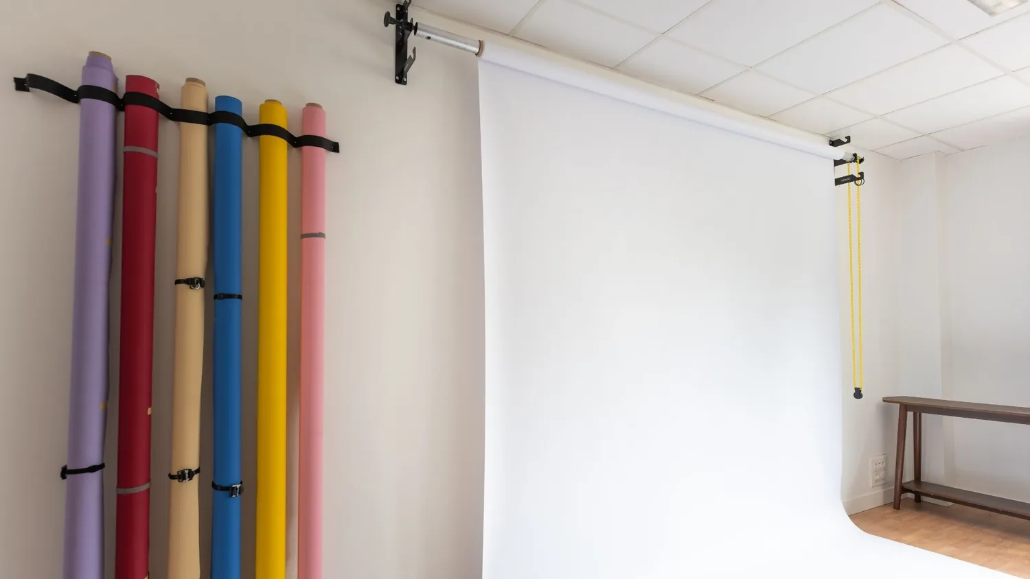 Rouleaux de fonds papier couleur accrochés au mur du studio, à côté du colorama blanc déroulé