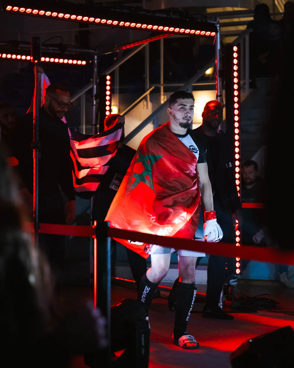 Combattant drapé dans un drapeau marocain montant vers la cage sous une lumière rouge