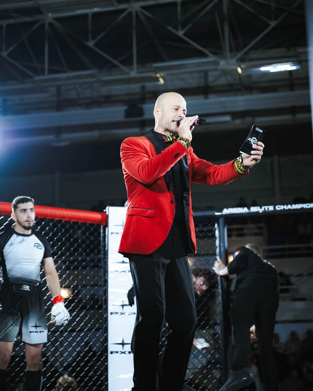 Speaker en veste rouge annonçant le combat au micro, à l’intérieur de la cage