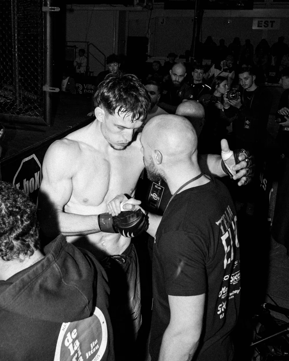 Photo en noir et blanc d’un combattant torse nu et de son coach avant le combat
