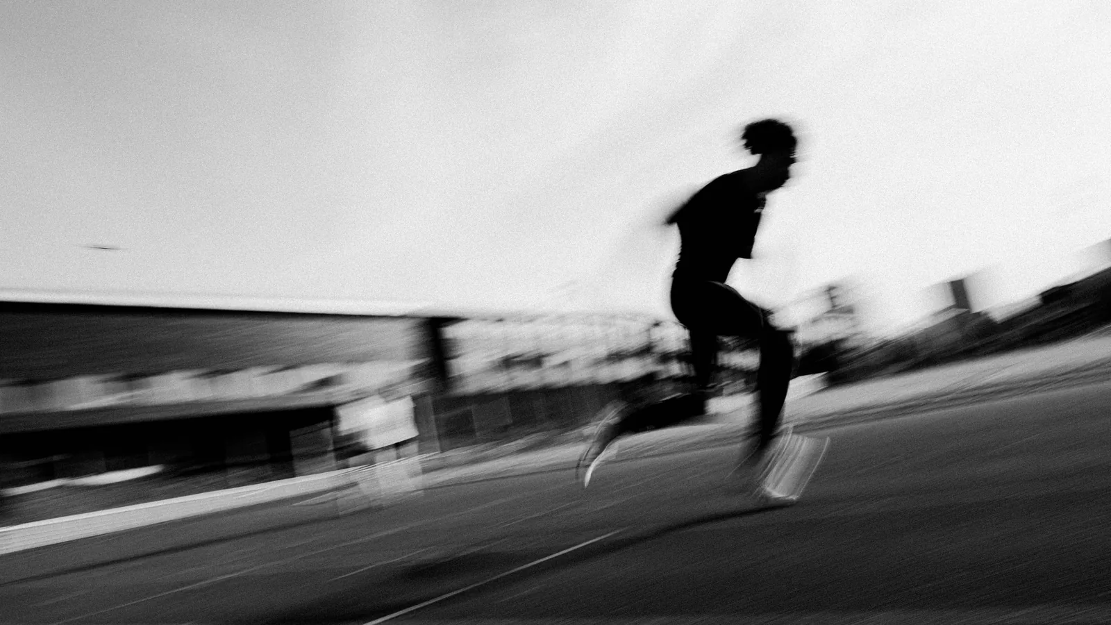 Coureur en pleine accélération sur une piste, filé de vitesse en noir et blanc
