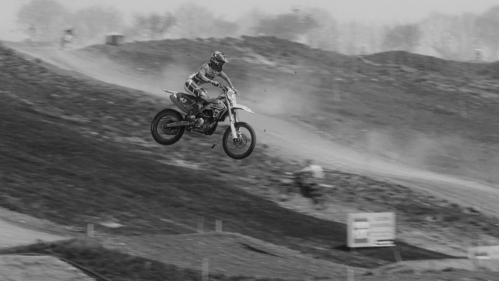 Pilote de motocross en l’air au sommet d’une butte, en noir et blanc