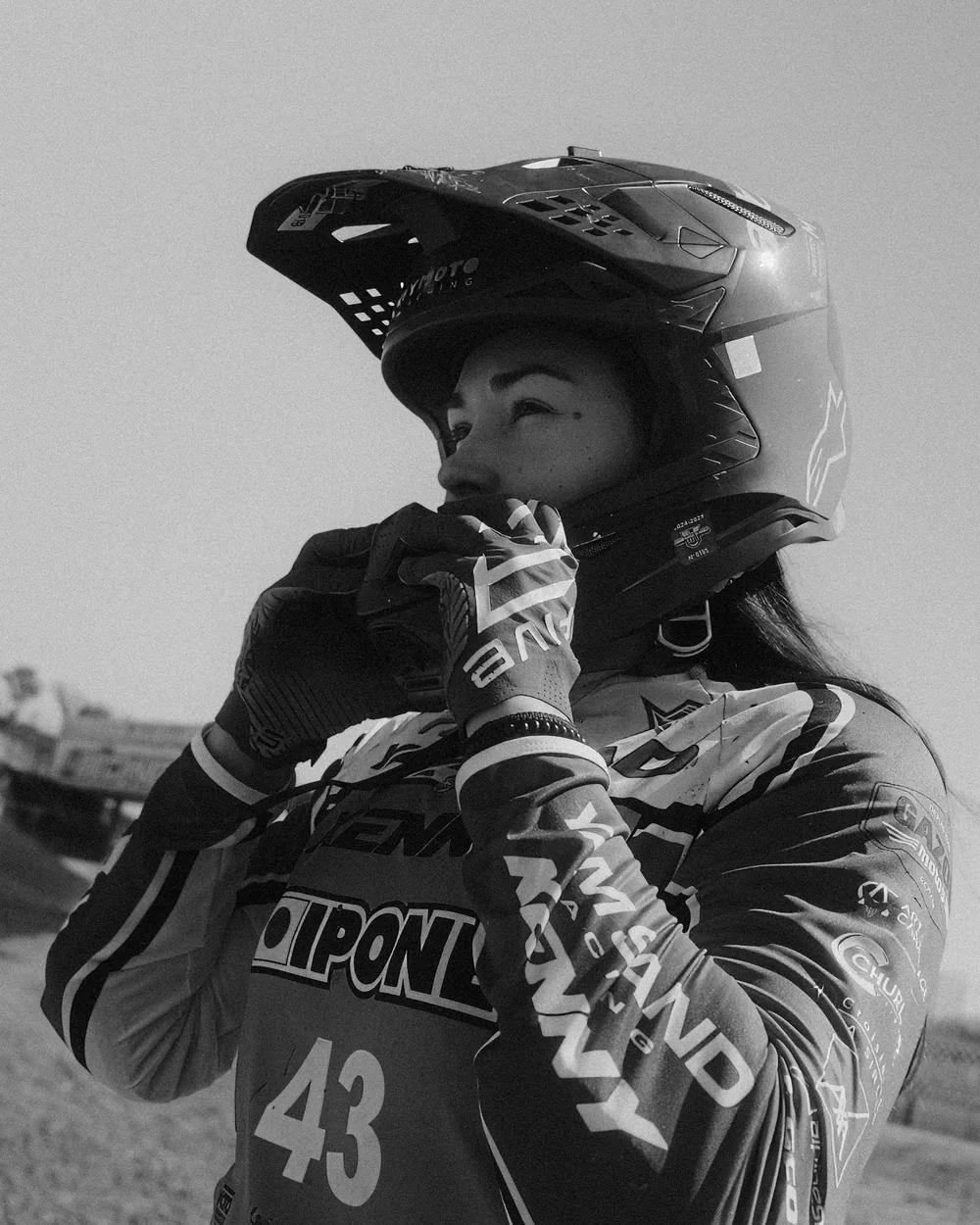 Pilote de motocross ajustant la jugulaire de son casque, en noir et blanc