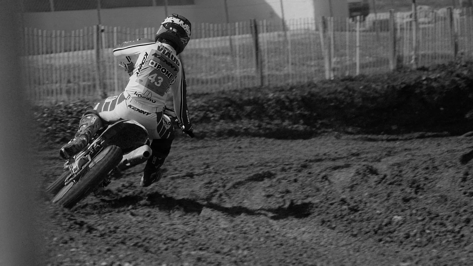 Pilote de motocross penché dans un virage terreux, en noir et blanc